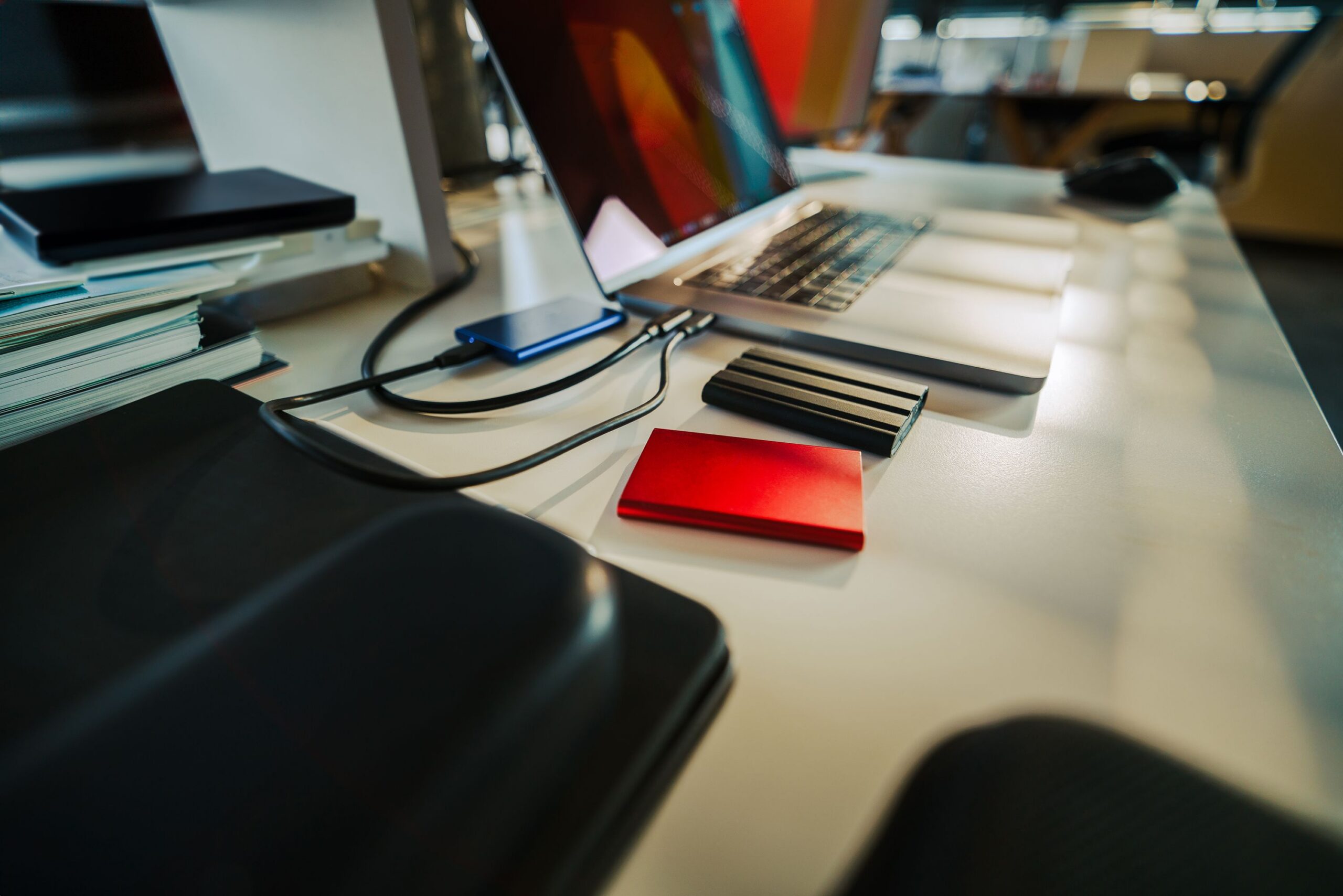 Close em uma mão segurando um smartphone com ícones de segurança digital sobre uma mesa de escritório.